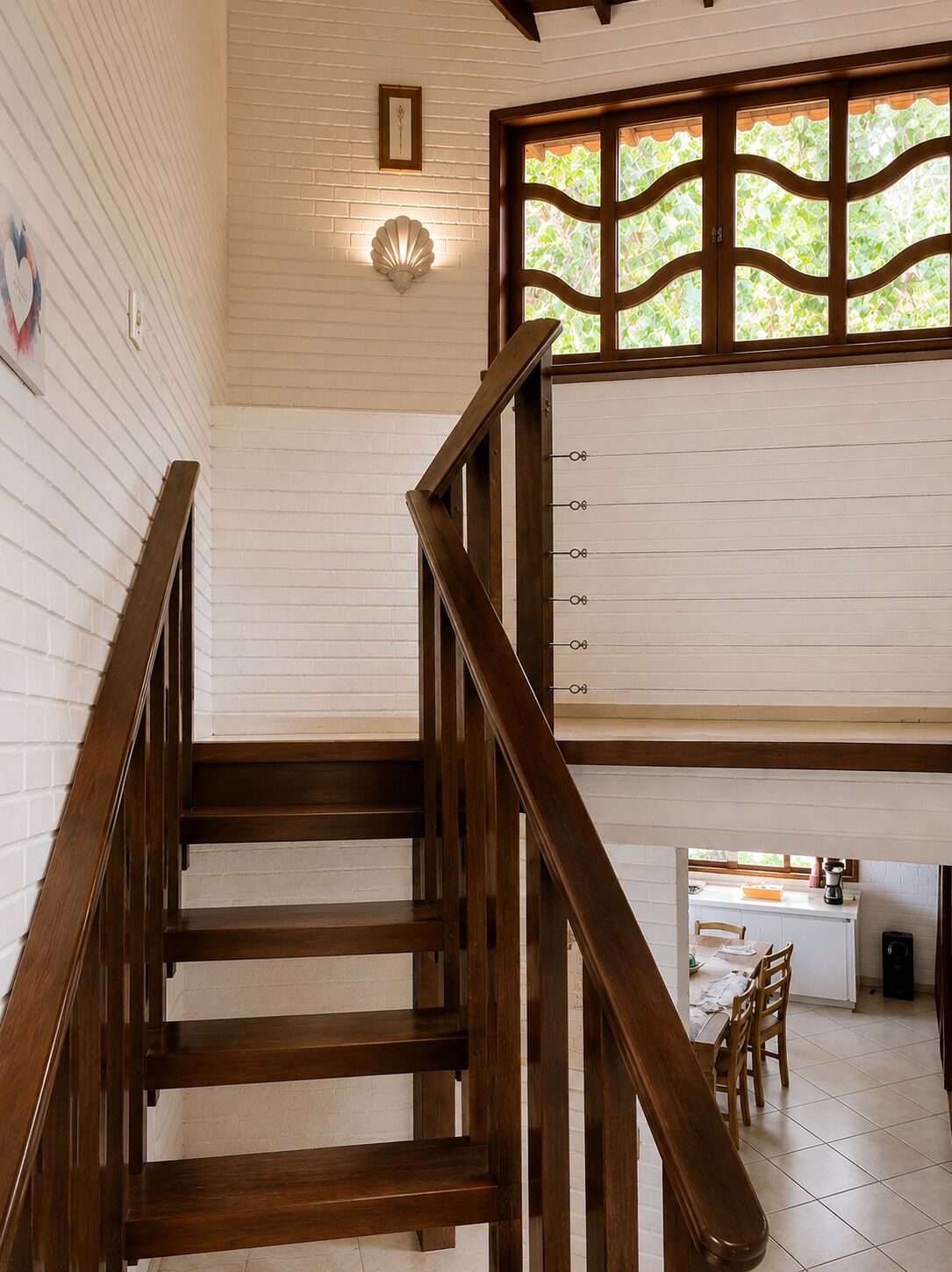 A wooden staircase leading to a room with a white brick wall, a decorative light fixture, and a window with a green view.