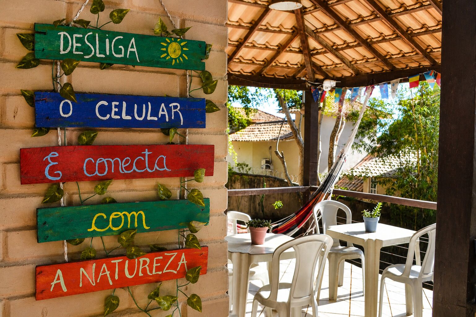 A wall with colorful signs and a patio area with a hammock, chairs, and potted plants.