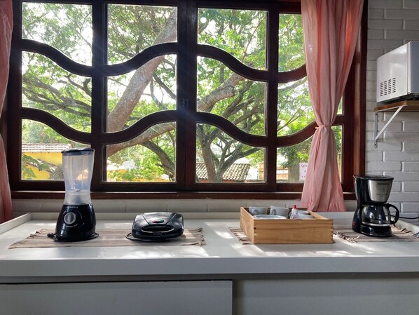 A kitchen with a window view of trees, a blender, a coffee maker, and a wooden box on the counter. - 5to Elemento House (Búzios)