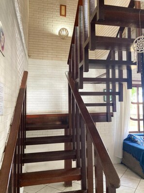 A wooden staircase with a white brick wall and a decorative shell light fixture on the ceiling. - 5to Elemento House (Búzios)