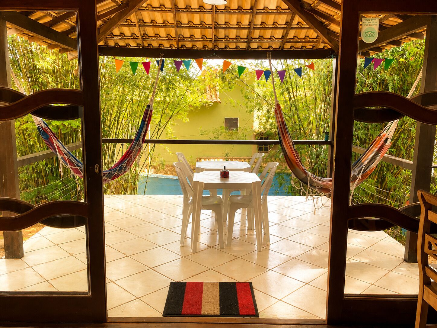 Un patio con mesa y sillas, rodeado de plantas de bambú y banderas coloridas.