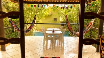Un patio con mesa y sillas, rodeado de plantas de bambú y banderas coloridas.