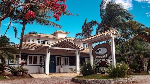 A two-story building with a tiled roof, a sign reading "Pousada," and tropical vegetation around it. - Hibiscus Center (Búzios)
