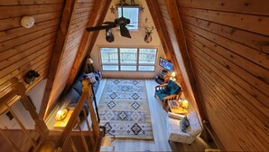 A high-ceilinged wooden interior with a loft area, a television, and a patterned rug. - Luther Secluded Riverfront A-Frame (Luther)