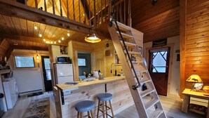 A wooden cabin interior with a kitchen, two stools, a ladder, and a window. - Luther Secluded Riverfront A-Frame (Luther)