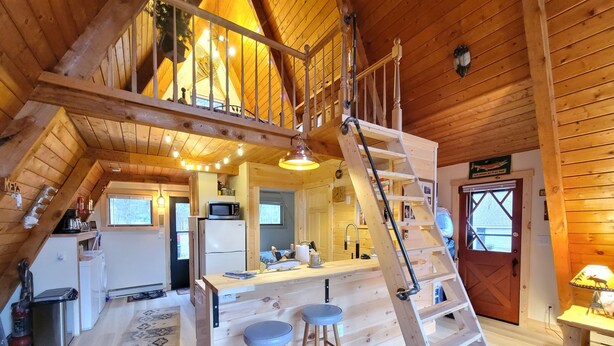 A cozy wooden cabin with a loft bedroom, a kitchen with modern appliances, and a dining area with stools. - Luther Secluded Riverfront A-Frame (Luther)