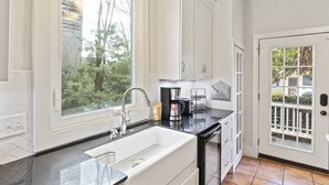 A kitchen with white cabinets, a black countertop, a sink, and a coffee maker. - Entire 4 Bedroom Historic Charleston House (Charleston)