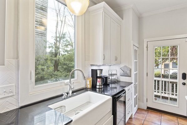 A kitchen with white cabinets, a black countertop, a sink, and a coffee maker.