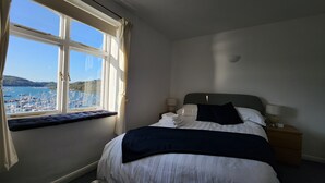 Et soveværelse med seng, et natbord, en lampe og et vindue med udsigt over en lystbådehavn.