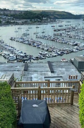 Un puerto deportivo con numerosas embarcaciones amarradas, vista del pueblo circundante y una cubierta de madera con mesa techada.