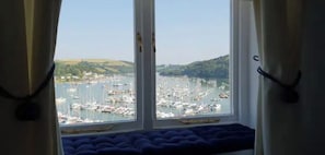 A view from a window with curtains, overlooking a marina with boats and hills in the distance.