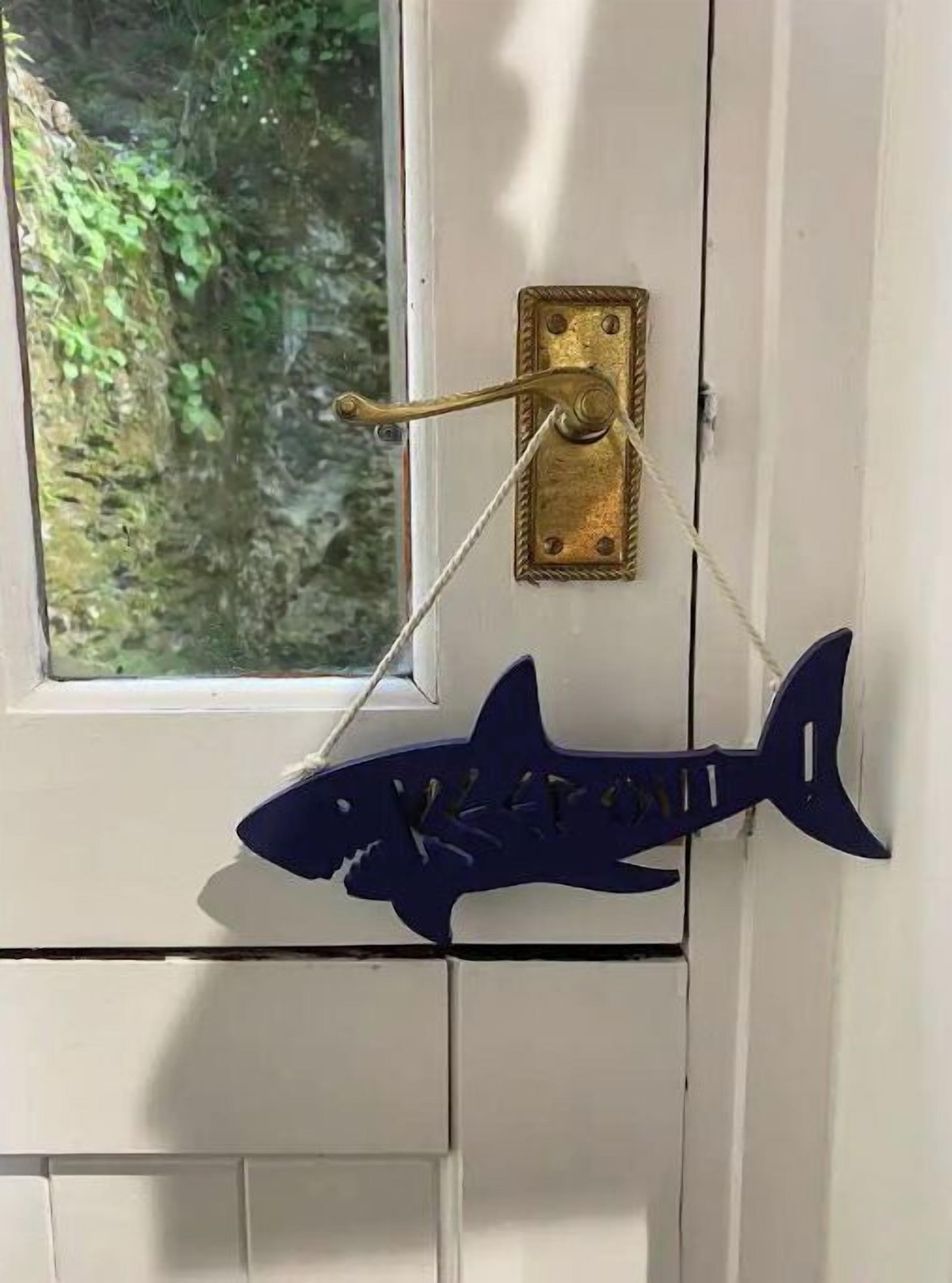 A door with a brass handle and a blue shark-shaped decoration hanging on it.