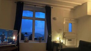 En stue med et stort vindue, fjernsyn, et lille bord med en lampe og en sofa.