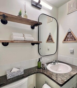 Une salle de bain avec un lavabo blanc, un miroir, des étagères en bois et un porte-serviettes.