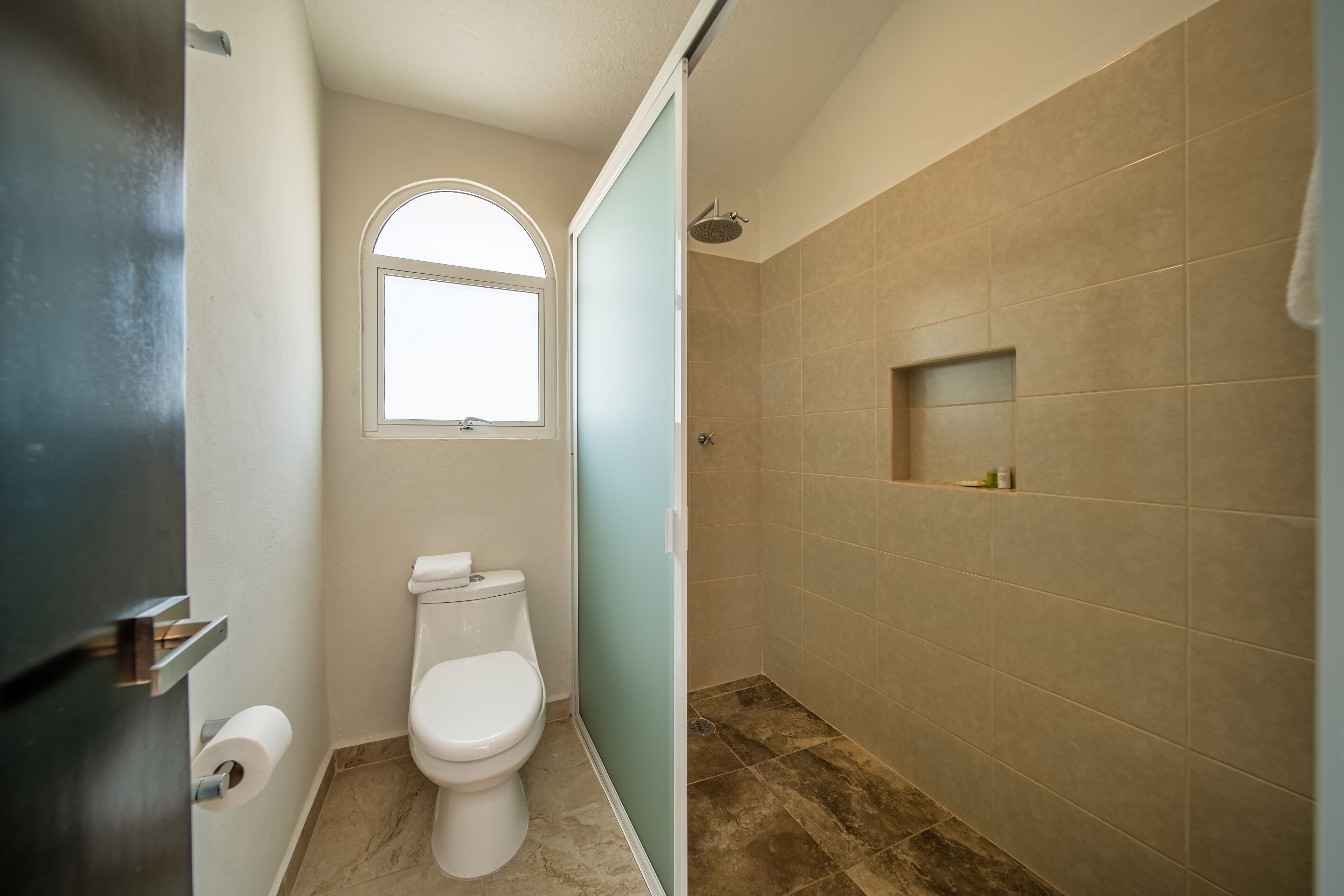Un baño con inodoro, ventana y zona de ducha con azulejos color beige.