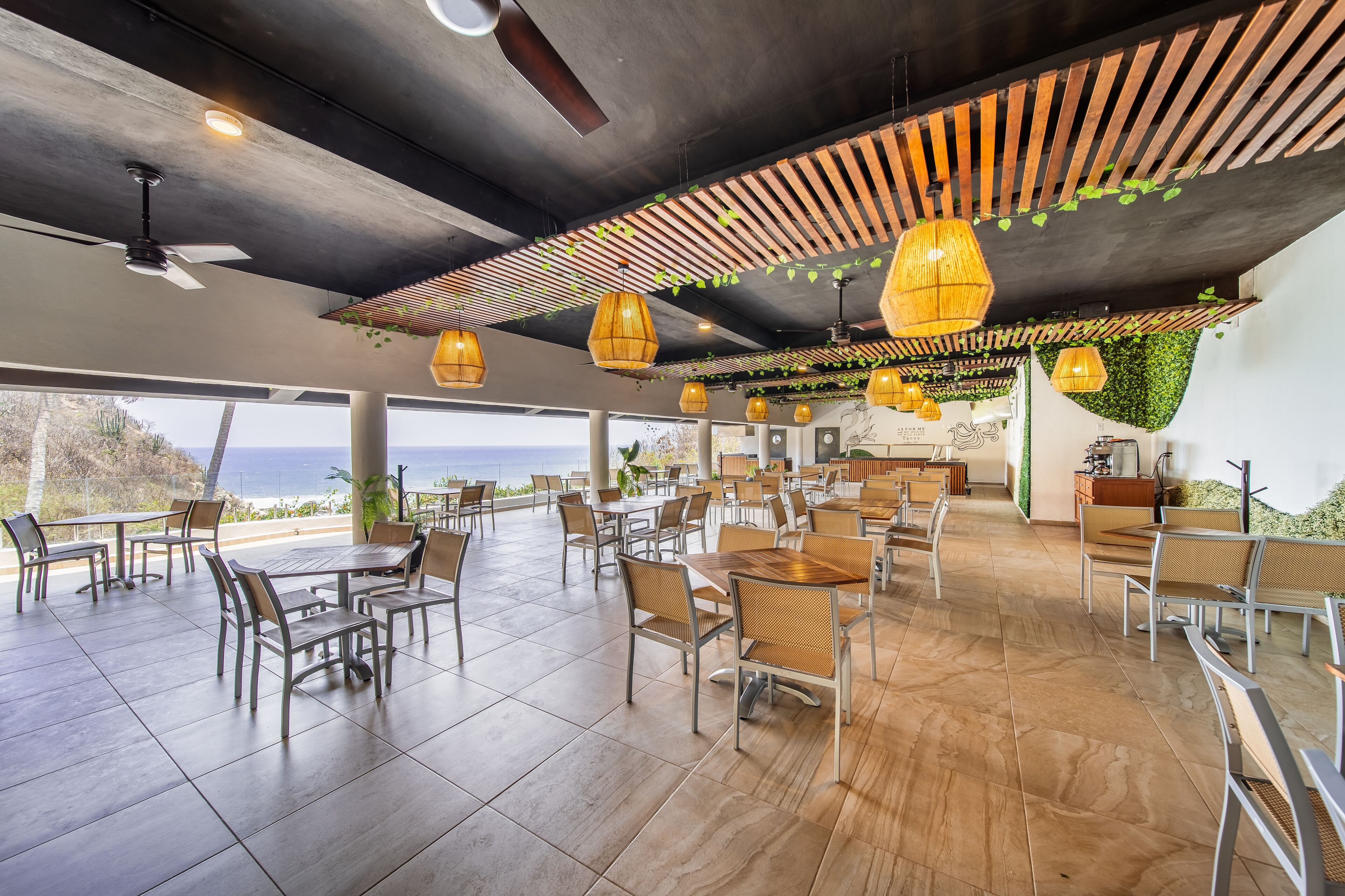 Amplia zona de comedor al aire libre con varias mesas y sillas, ventilador de techo e iluminación colgante.