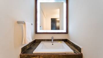 Un baño con lavamanos blanco, un espejo y un perchero para toallas.