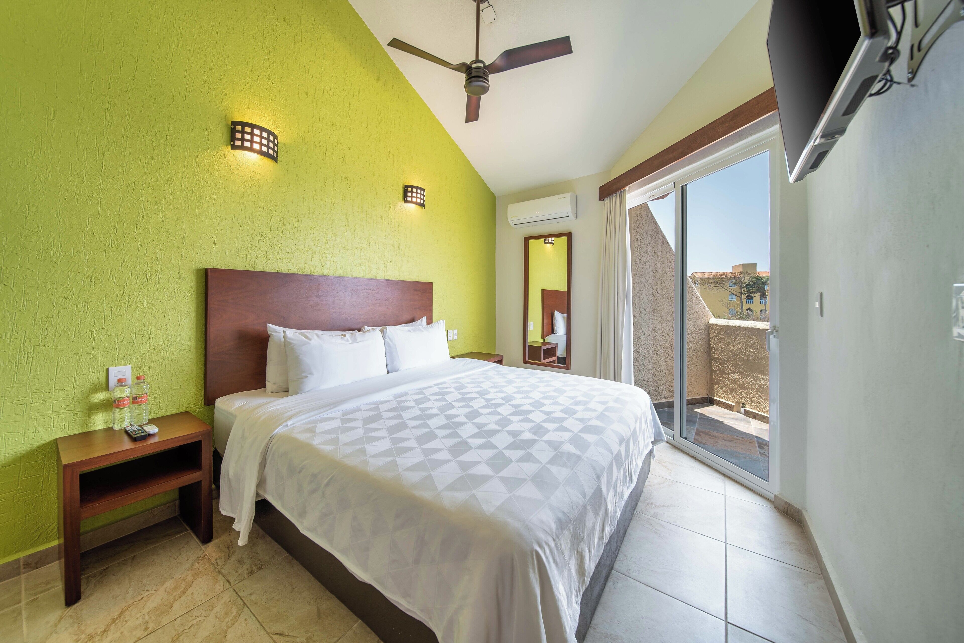 Une chambre d’hôtel avec un lit, une table de chevet et une vue sur l’extérieur, accessible par une porte-fenêtre coulissante.