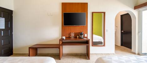 A hotel room with two beds, a wooden desk with a flat-screen TV, a mirror, and a door leading to a balcony.