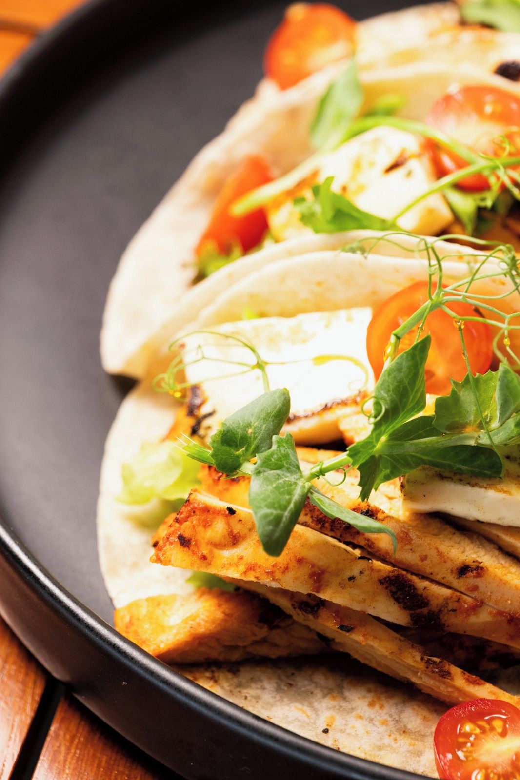 Ein Teller mit drei Tacos, gefüllt mit gegrilltem Hähnchen, Salat und Tomatenscheiben.