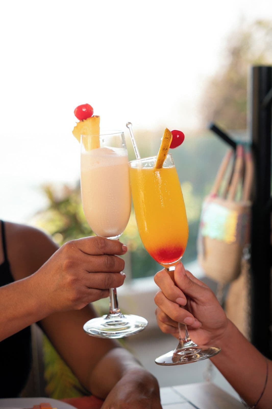 Two people holding cocktail glasses with fruit garnishes.