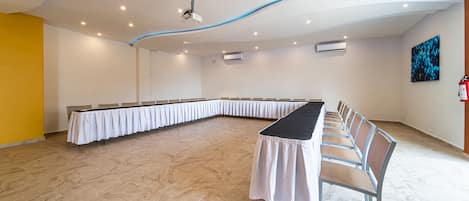 Une salle de conférence équipée d’une longue table et de chaises, de climatiseurs et d’un projecteur au plafond.