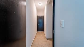Un couloir étroit, avec une porte sombre au fond, des murs blancs et un interrupteur sur le côté droit.