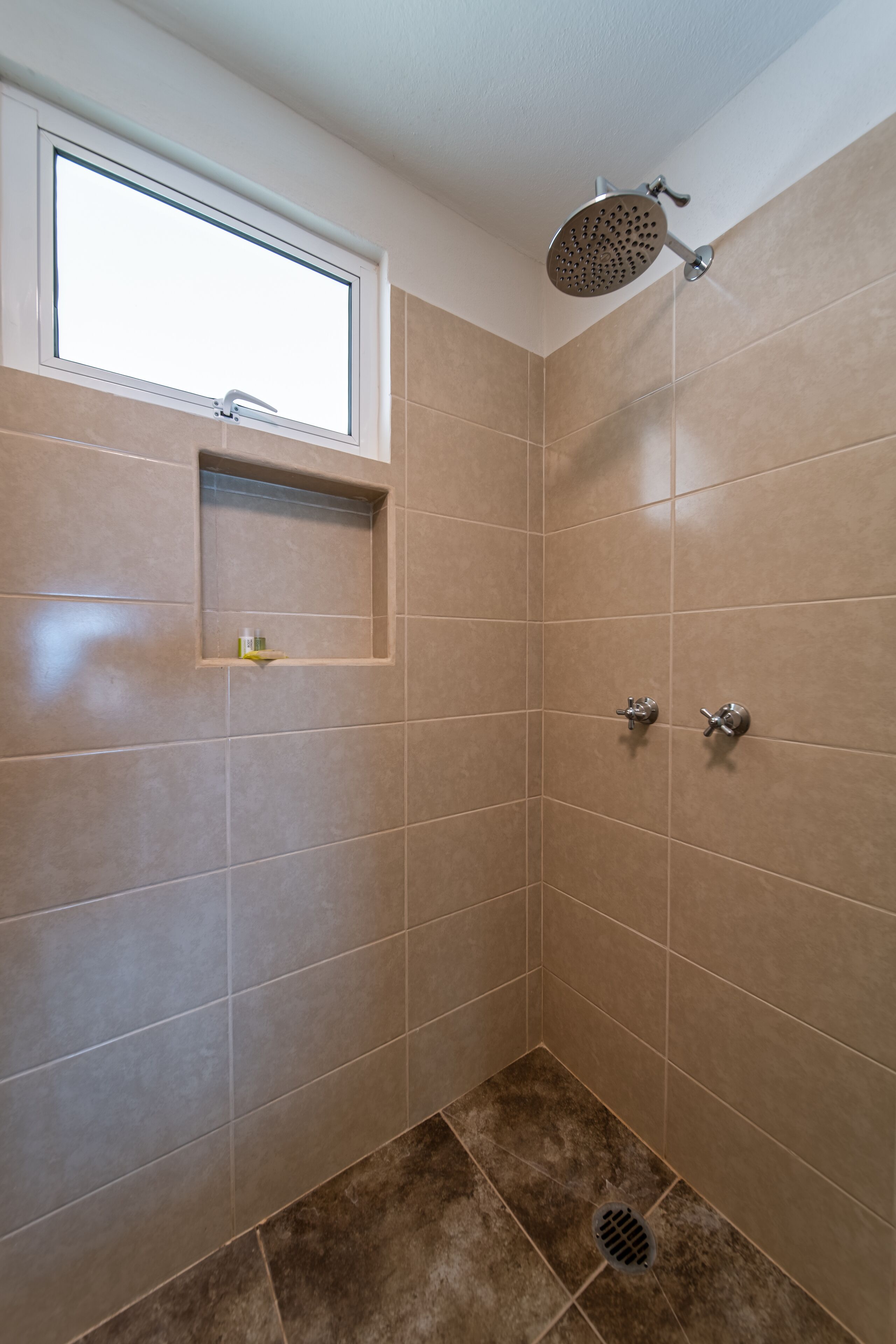 Un baño pequeño con azulejos, una ventana, un estante y dos cabezales de ducha.