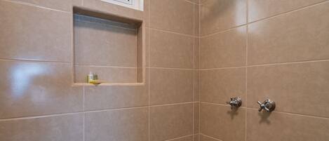Un baño pequeño con azulejos, una ventana, un estante y dos cabezales de ducha.