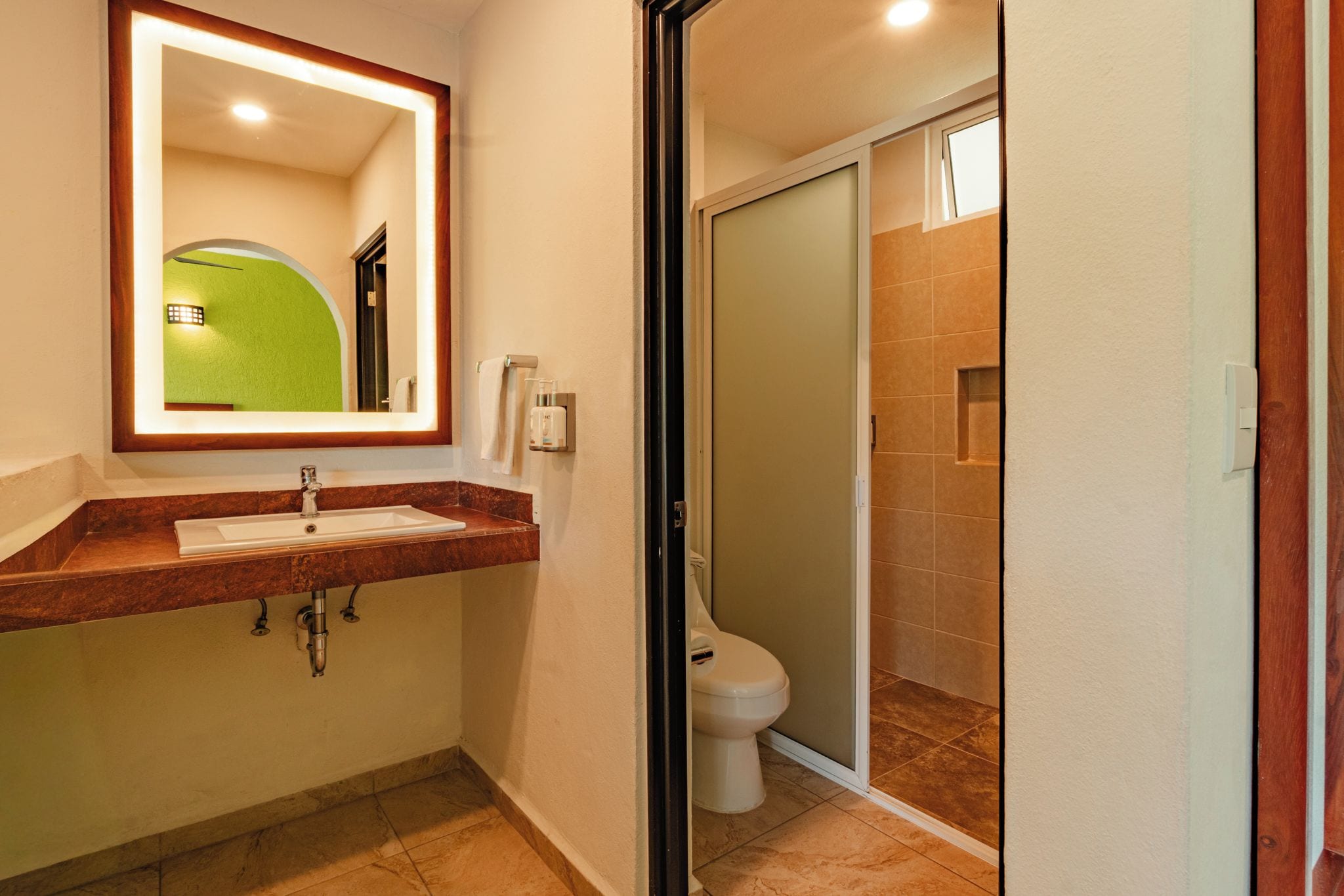 A bathroom with a sink, mirror, toilet, and shower area.