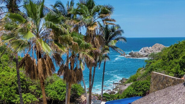 A resort with a pool area, palm trees, and a view of the ocean. - Villas Coral Huatulco (Santa María Huatulco)