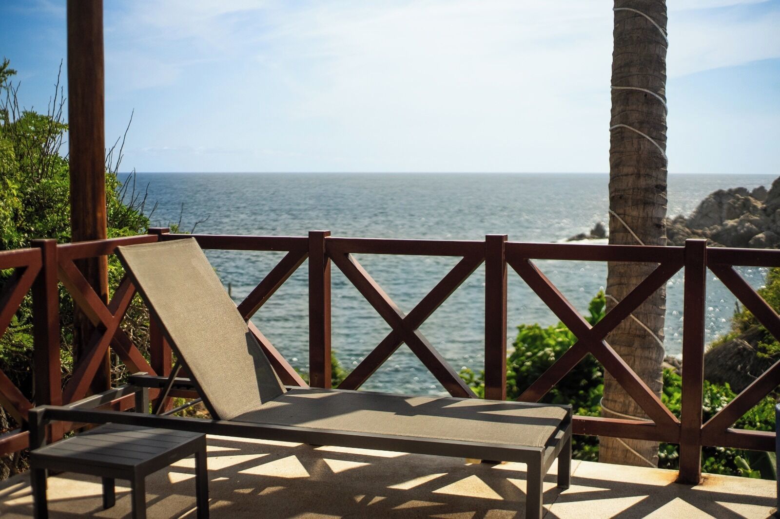 A beachside lounge with a view of the ocean, featuring a wooden railing and a single lounge chair.