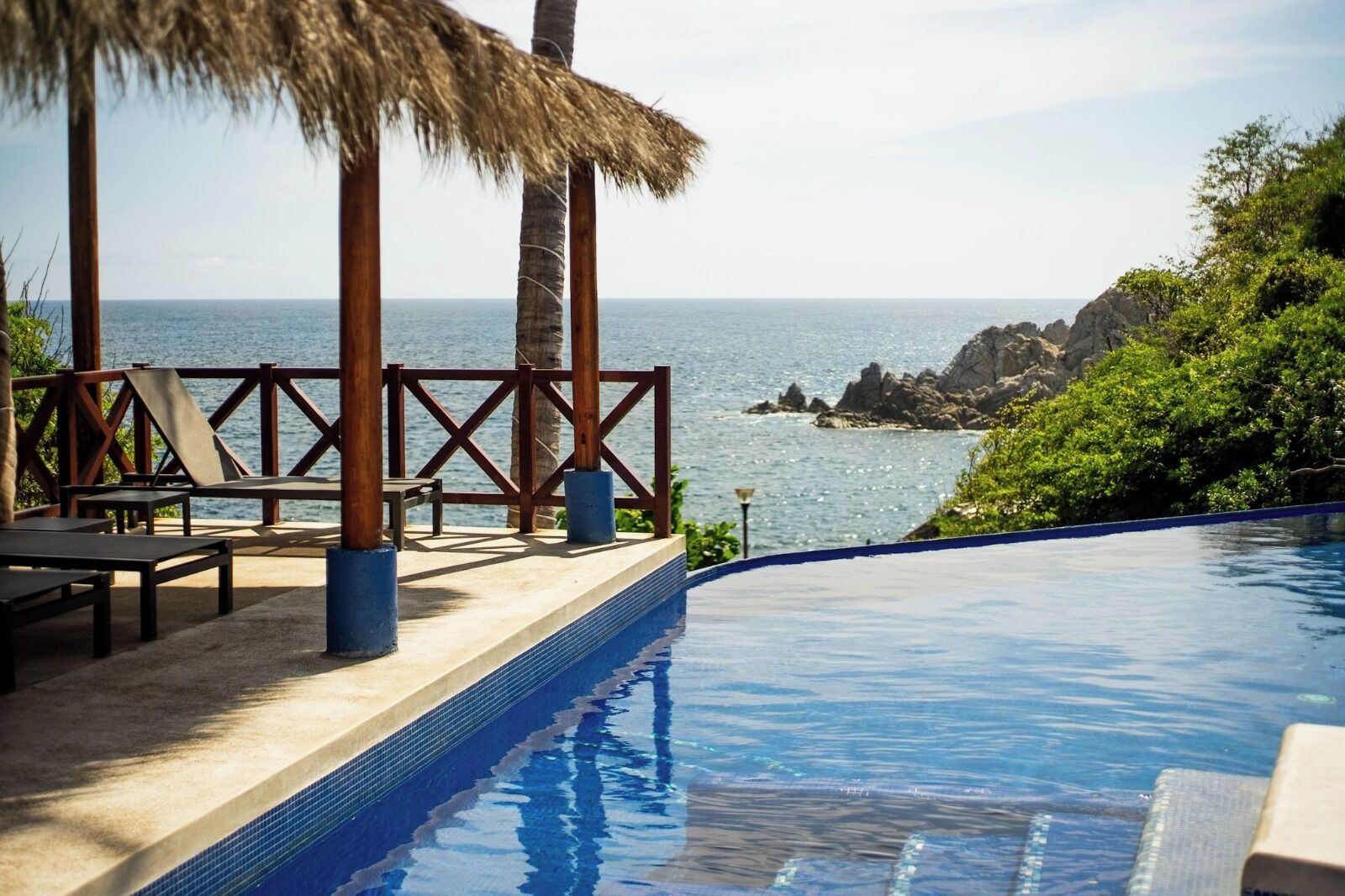 Zona de piscina con sillones de descanso y una estructura de techo de paja con vistas al mar.