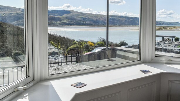 A room with a large window overlooking a coastal landscape with hills and a beach. - 2 bedroom accommodation in Barmouth (Barmouth)
