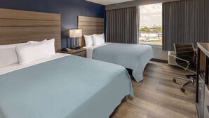 A hotel room with two beds, a desk, a chair, and a window with a view of the city. - Baymont by Wyndham Laredo (Laredo)