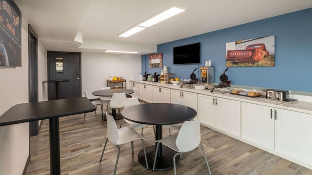 A modern kitchen with white cabinets, a black countertop, and a round dining table with white chairs. - Baymont by Wyndham Laredo (Laredo)