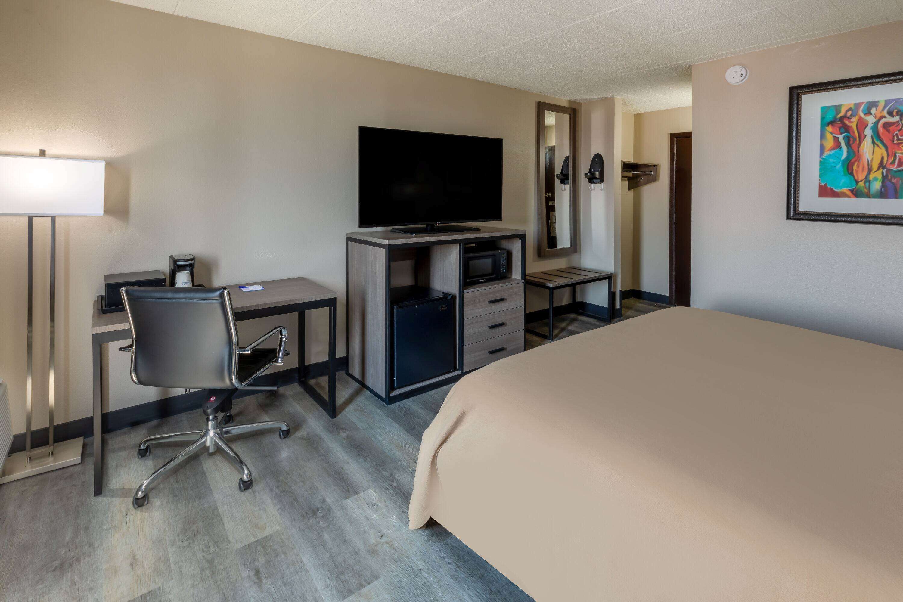 Een hotelkamer met een bed, een bureau met een computer, een televisie, een magnetron en een koffiezetapparaat.