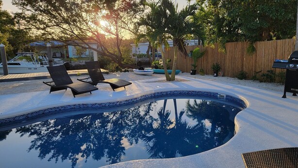 A swimming pool with lounge chairs, a wooden fence, and a boat dock. - Gorgeous 3/2 SFH brand-new pool & spa,30ft dockage (Marathon)