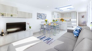 Ett modernt vardagsrum med en platt-TV, en soffa och en matplats med ett glasbord.