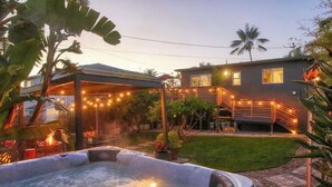 Ein Whirlpool in einem Garten mit überdachter Terrasse, ein Haus mit Balkon und einer Rasenfläche.