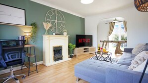 Ein Wohnzimmer mit Kamin, Fernseher, einer Couch und einem Schreibtisch mit Computer.