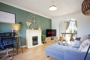 A living room with a fireplace, a TV, a sofa, and a desk with a computer.