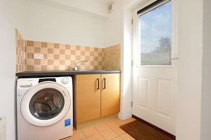 A compact laundry room with a washing machine, wooden cabinets, and a window.