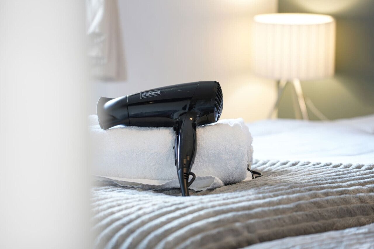 A hair dryer on a white towel on a bed with a textured blanket.
