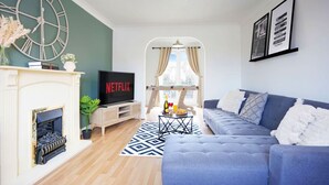 Ein Wohnzimmer mit Kamin, Fernseher, einer Couch und einer großen Wanduhr.