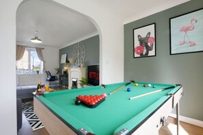 A pool table in a room with a fireplace, a clock, and framed artwork on the wall.