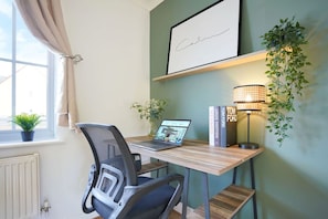 A workspace with a laptop, a chair, a desk, a lamp, and a framed picture on the wall.