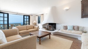 Un salón amplio con chimenea, ventanas grandes y vista al mar.