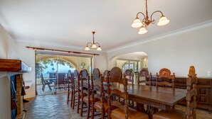 Un comedor espacioso con una gran mesa de madera y sillas a juego, un piso con diseño en espiga y una araña.