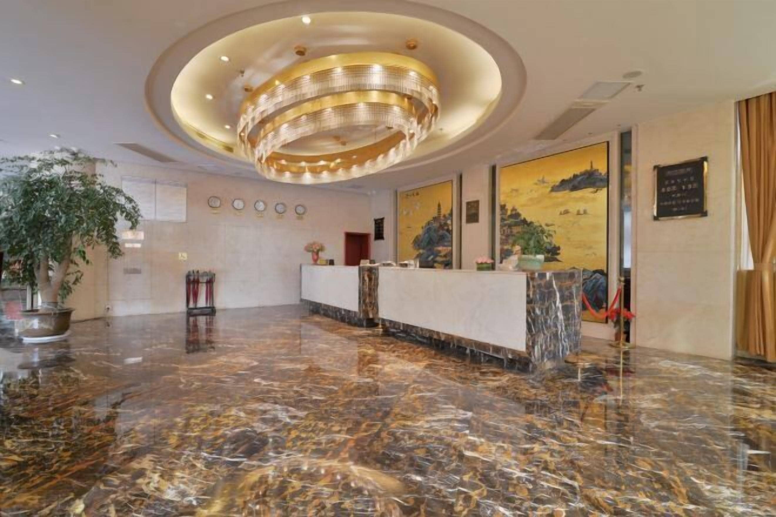 A lobby with a marble floor, a reception desk, a large chandelier, and framed artwork on the walls.